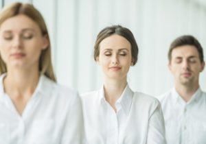 Office employees practicing mindfulness meditation with eyes closed during a corporate wellness session.